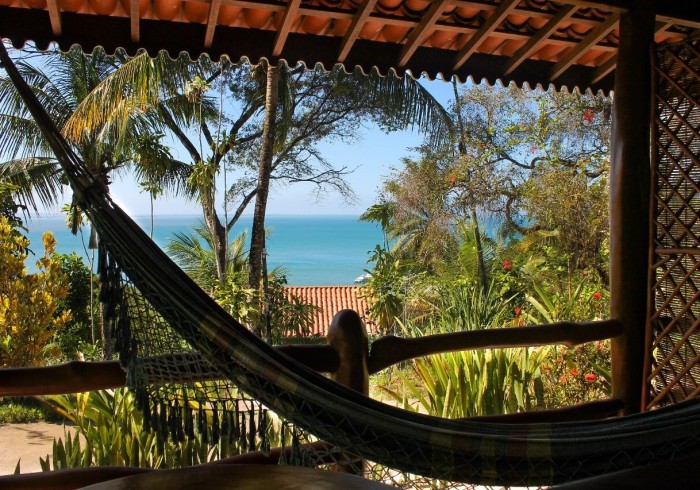 Rede em uma varanda com vista para o mar entre as palmeiras.