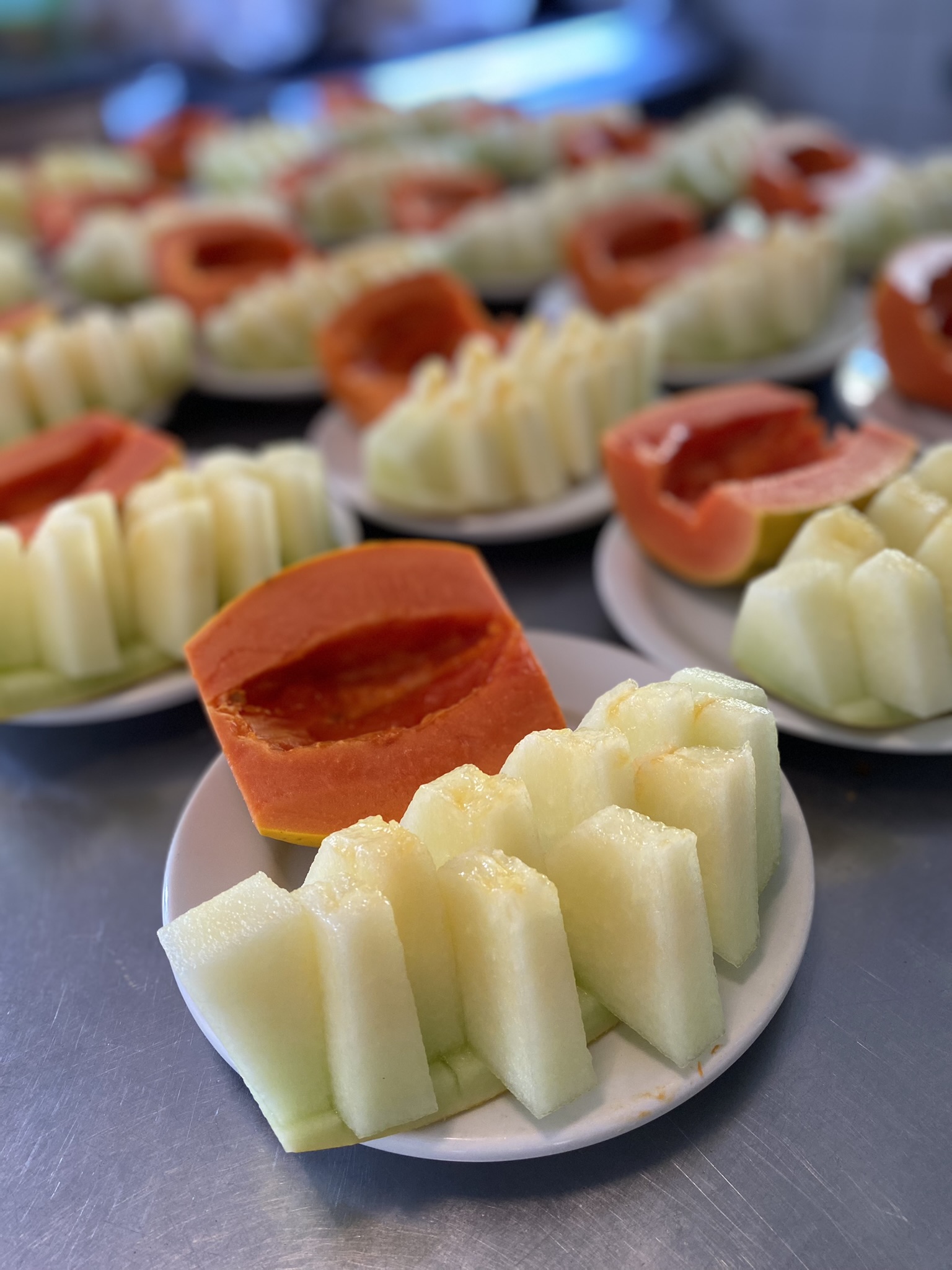 Pratos individuais com mamão e melão fatiados, preparados para o café da manhã