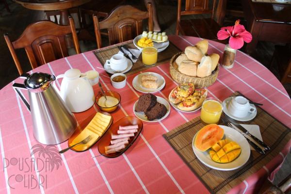 Mesa posta com café da manhã completo: pães, frutas, presunto, queijo, ovos e suco de laranja