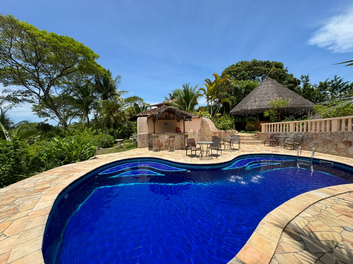Piscina da pousada cercada por árvores e áreas de descanso.